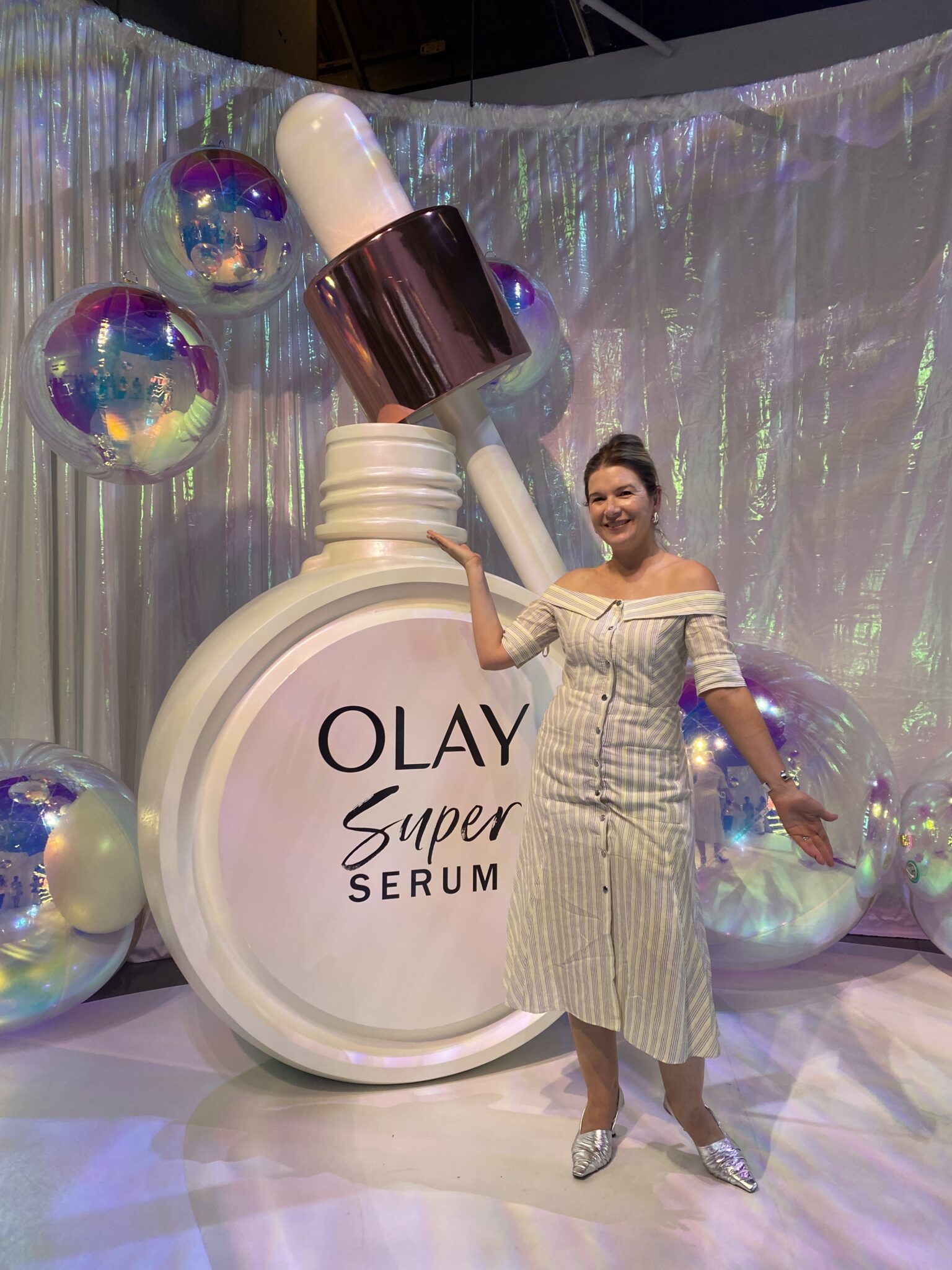Woman standing next to life size OLAY Super Serum bottle and dropper